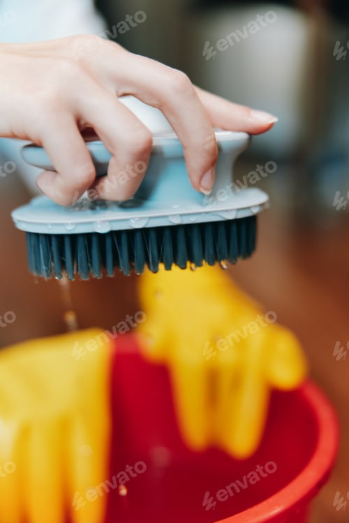 Preview: Person in yellow gloves using brush to clean red bowl with yellow sponge inside