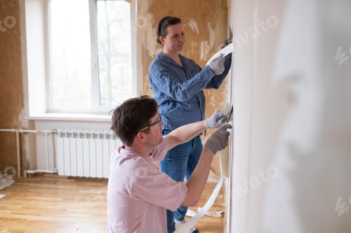 Preview: Young couple removing old wallpaper from walls preparing for flat renovation.