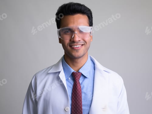 Preview: Face of happy young Indian man doctor with protective glasses smiling