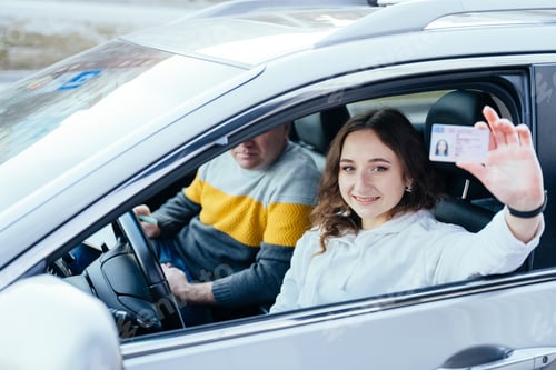 Preview: Happy young caucasian woman driving her new car holding car license.