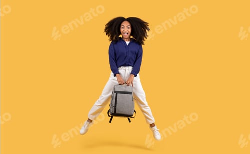 Preview: Excited black student lady with backpack jumping on a yellow background