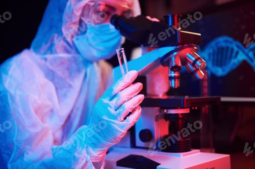 Preview: Nurse in mask and white uniform, holding tube with liquid and sitting in neon lighted laboratory