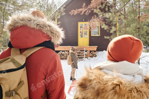 Preview: Rear view of young couple with backpacks and their little son with sledge