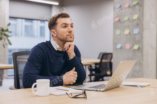 Preview: Professional businessman sitting at desk, resting chin on hand, gazing pensively while deep
