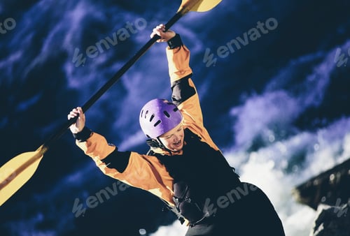 Preview: Female whitewater kayaker holding a paddle above her head, river rapids in the background