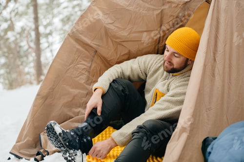 Preview: Man putting on winter boot inside tent camping