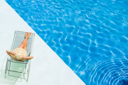 Preview: beautiful woman in a hat sitting on the edge of the pool