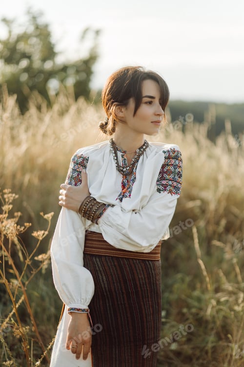 Preview: Young woman in traditional national embroidered shirt and skirt on nature at sunset.