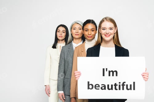 Preview: smiling multicultural businesswomen near placard with i`m beautiful lettering isolated on white