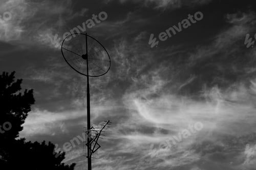 Preview: Grayscale shot of a satellite dish and TV antenna in the dramatic sky background