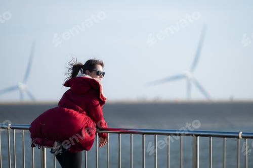 Preview: On the background of windmills, A young woman in a red jacket is enjoying her winter vacation.