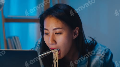 Preview: Freelance business women eating instant noodles tired while working on laptop at home at night.