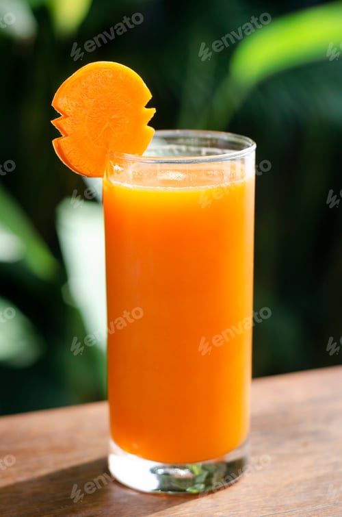 Preview: glass of fresh organic carrot juice on garden table outdoors