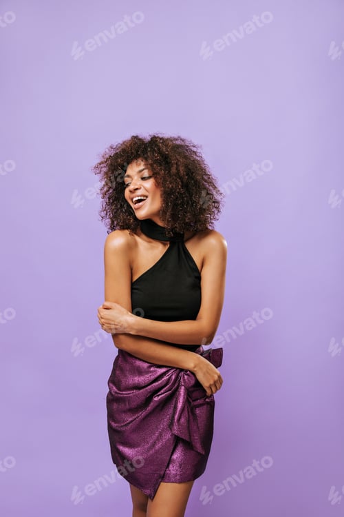 Preview: Stylish lady in black top and shiny short skirt poses on isolated background. Girl with curly hair