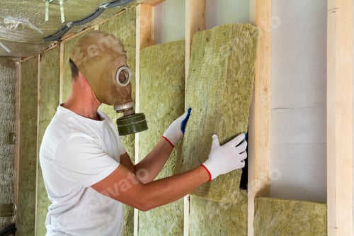 Preview: Young worker in gas mask insulating rock wool insulation staff in wooden frame