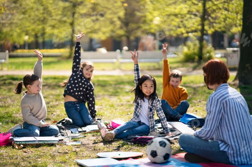 Preview: Teacher with small children sitting outdoors in city park, learning group education concept