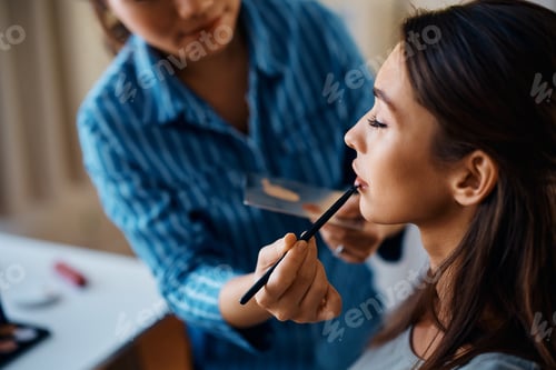 Preview: Close up of makeup artist applying lipstick with a brush on woman's lips.