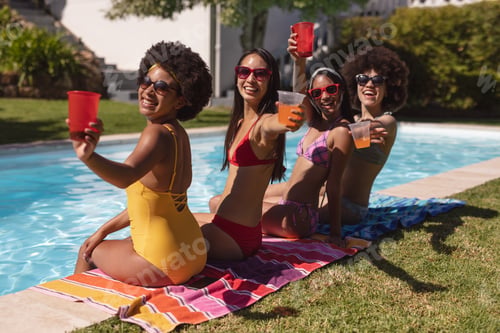 Preview: Diverse group of female friends drinking drinks sitting at the poolside