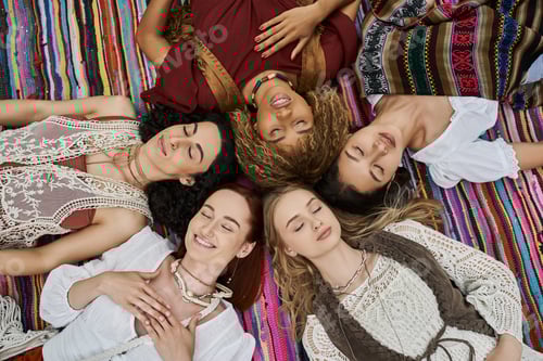 Preview: top view of smiling multiethnic women in boho outfits lying on blanket in retreat center