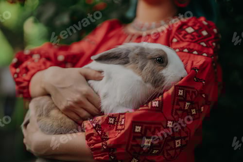 Preview: Ukrainian Woman holding cute bunny rabbit on hands. Lady In Traditional Outfit.