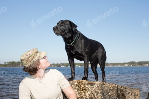 Preview: Female soldier with labrador dog on lakeside rock