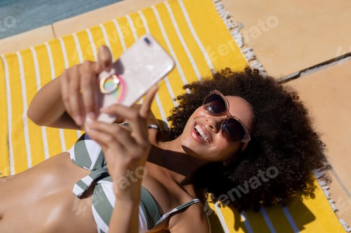 Preview: Young woman using mobile phone near swimming pool