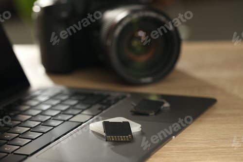Preview: SD memory cards, holder, laptop and photo camera on wooden table, closeup