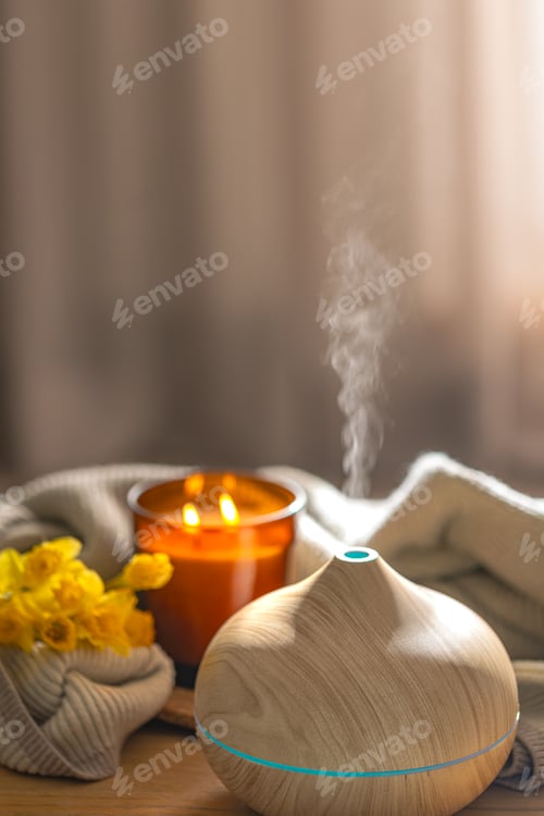 Preview: Wood aroma diffuser producing mist in cozy spa interior with candle and flowers. Wellness relaxation