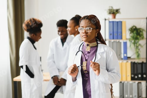 Preview: Confident female doctor in front of team, looking at camera smiling