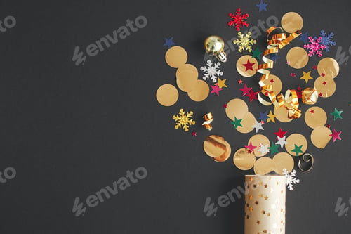 Preview: Modern colorful confetti popping from golden wrapping paper on black background, new year flat lay