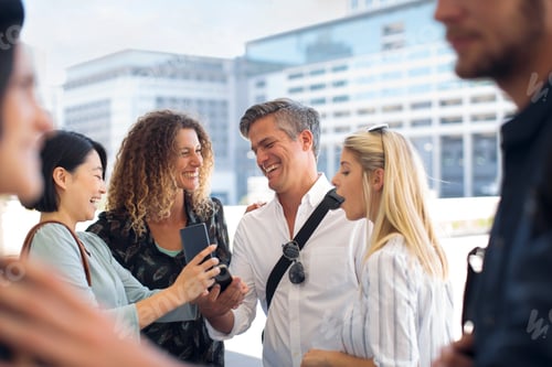 Preview: Group of happy casual businesspeople sharing cell phone on urban square
