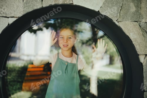Preview: Little girl standing behing round window, looking outside.