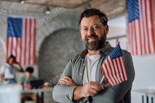 Preview: Happy citizen holding national flag at polling place during US elections and looking at camera.