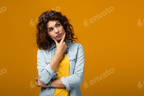 Vista previa: pensive redhead woman thinking while standing on orange