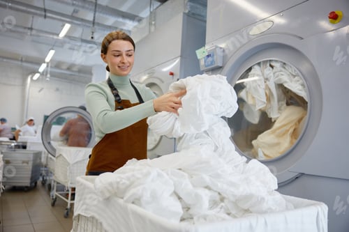 Preview: Female worker is loading clothes into a washing machine at a laundromat