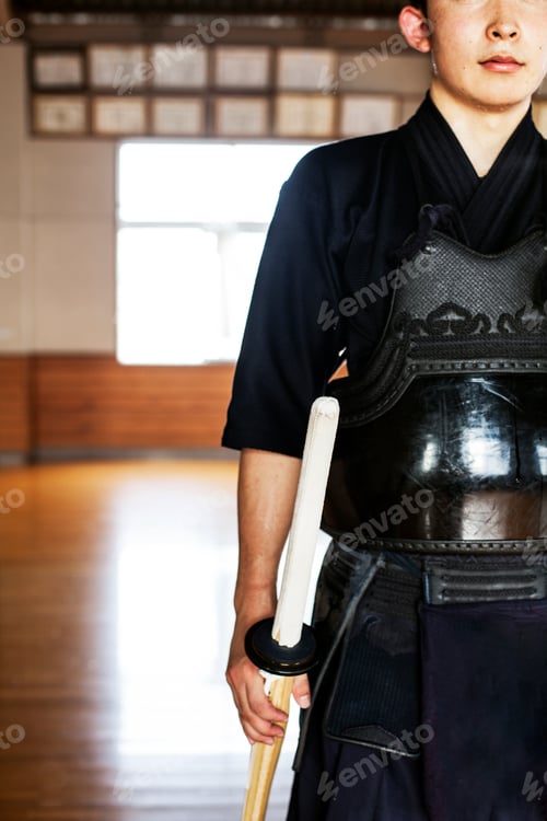 Preview: Male Japanese Kendo fighter standing in a gym, holding wood sword.