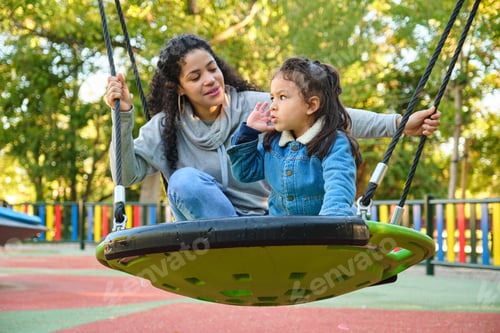 Preview: Latin mother playing with her son on a swing in a park.