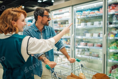 Preview: Supermarket employee helping customer choosing frozen food from refrigerator shelves