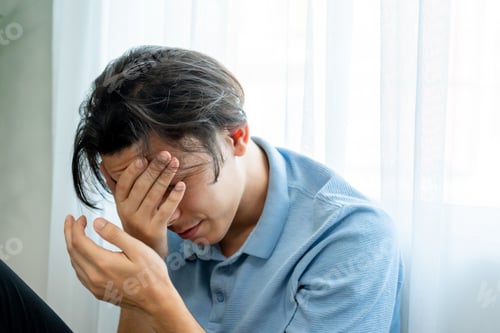 Preview: Asian upset depressed man sitting alone on floor in living room at home.
