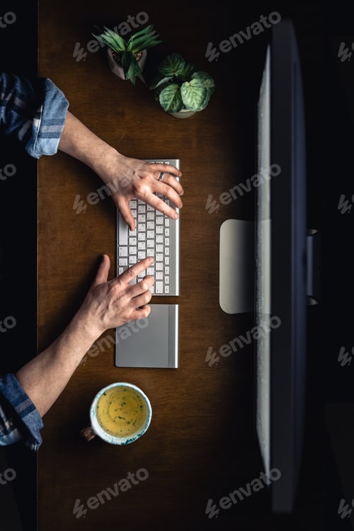 Preview: Top view of a man working at a computer in a dark room at night.