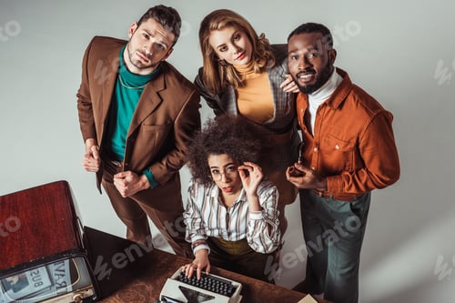 Preview: overhead view of multicultural retro styled friends with typewriter looking at camera