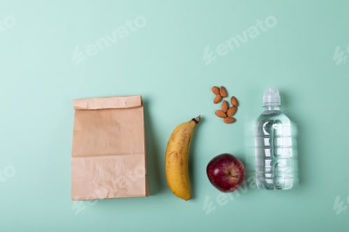 Preview: Directly above shot of paper lunch bag with fruits, almonds and water bottle on green background