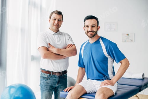 Preview: smiling Physiotherapist and football player in hospital looking at camera
