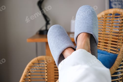 Preview: Closeup of a woman wearing slippers, laying and putting legs on wooden chair