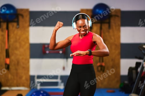 Preview: Motivated athlete monitoring fitness progress, enjoying workout with headphones in modern gym