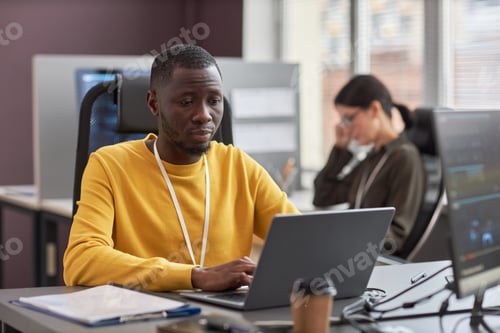 Preview: Young black man using laptop while working as software developer in IT company