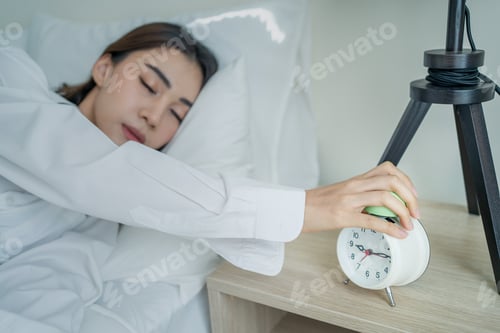 Preview: Asian beautiful tired young woman turn off sound ringing of an alarm clock in morning on bed