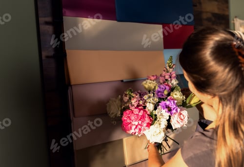 Preview: Young woman working in her flower shop choosing wrapping paper for bouquet.