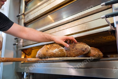 Preview: Male employee baker of bakery in workshop workshop of artisan bakery baking loaves in oven