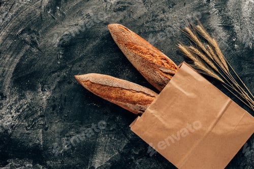 Preview: top view of arranged french baguettes in paper bag and wheat on dark tabletop with flour